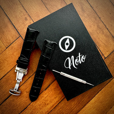 Black leather watch strap with tool on a black notebook with 'Noto' branding on a wooden surface